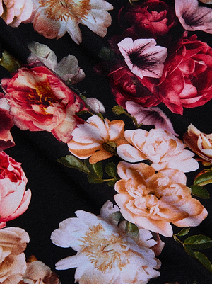 A close-up of the Tess Long-Sleeve Tee by L'AGENCE, showcasing luxe microfiber fabric with a floral print featuring large pink, red, peach, and white flowers with green leaves on a black background.
