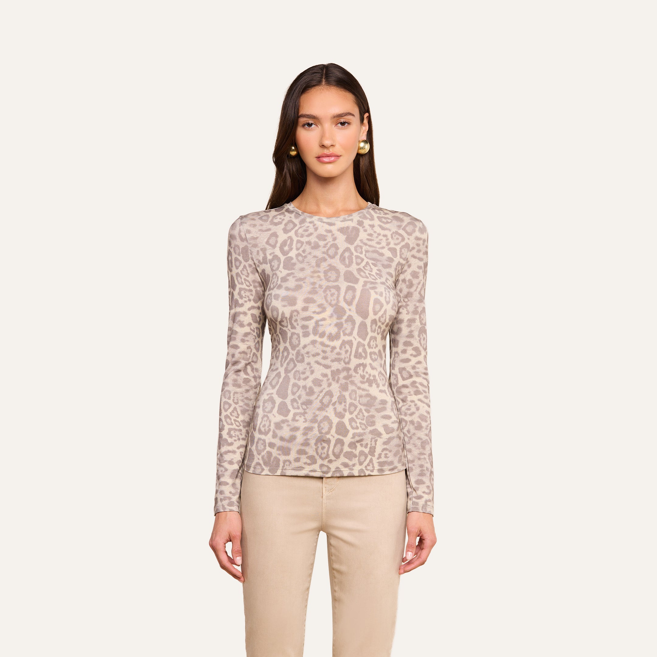 A woman wears the Tess Long Sleeve Tee, featuring a slim fit and subtle grey leopard print, paired with beige pants and set against a plain off-white background.