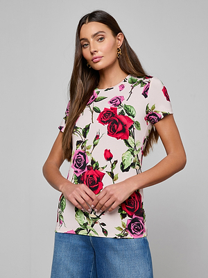 A woman with long brown hair wears the Ressi Fitted Tee, a slim-cut, short-sleeve white top with a colorful rose print, paired with blue jeans against a plain light gray background.