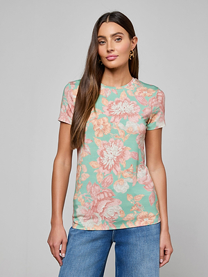 A woman with long brown hair wears the Ressi Fitted Tee in mint green with a pink floral print, paired with blue jeans, standing against a plain light gray background.
