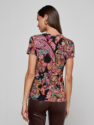 A woman with long brown hair wears gold hoop earrings and the L’AGENCE Ressi Fitted Tee, a multicolored paisley print stretch jersey knit top, paired with brown pants, shown from the back against a light gray background.