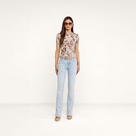 A woman stands facing forward against a plain white background, wearing sunglasses, heels, a belt, light blue jeans, and the Ressi Fitted Tee—a slim cut short-sleeve patterned top.
