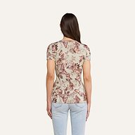 A woman with long brown hair, wearing the beige floral-patterned Ressi Fitted Tee and light blue jeans, stands with her back to the camera against a plain light background.