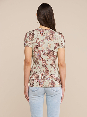 A woman with long brown hair stands with her back to the camera against a beige background, wearing the bestselling Ressi Fitted Tee—a short-sleeve, beige t-shirt with a pink and brown butterfly print—in soft stretch jersey knit and light blue jeans.