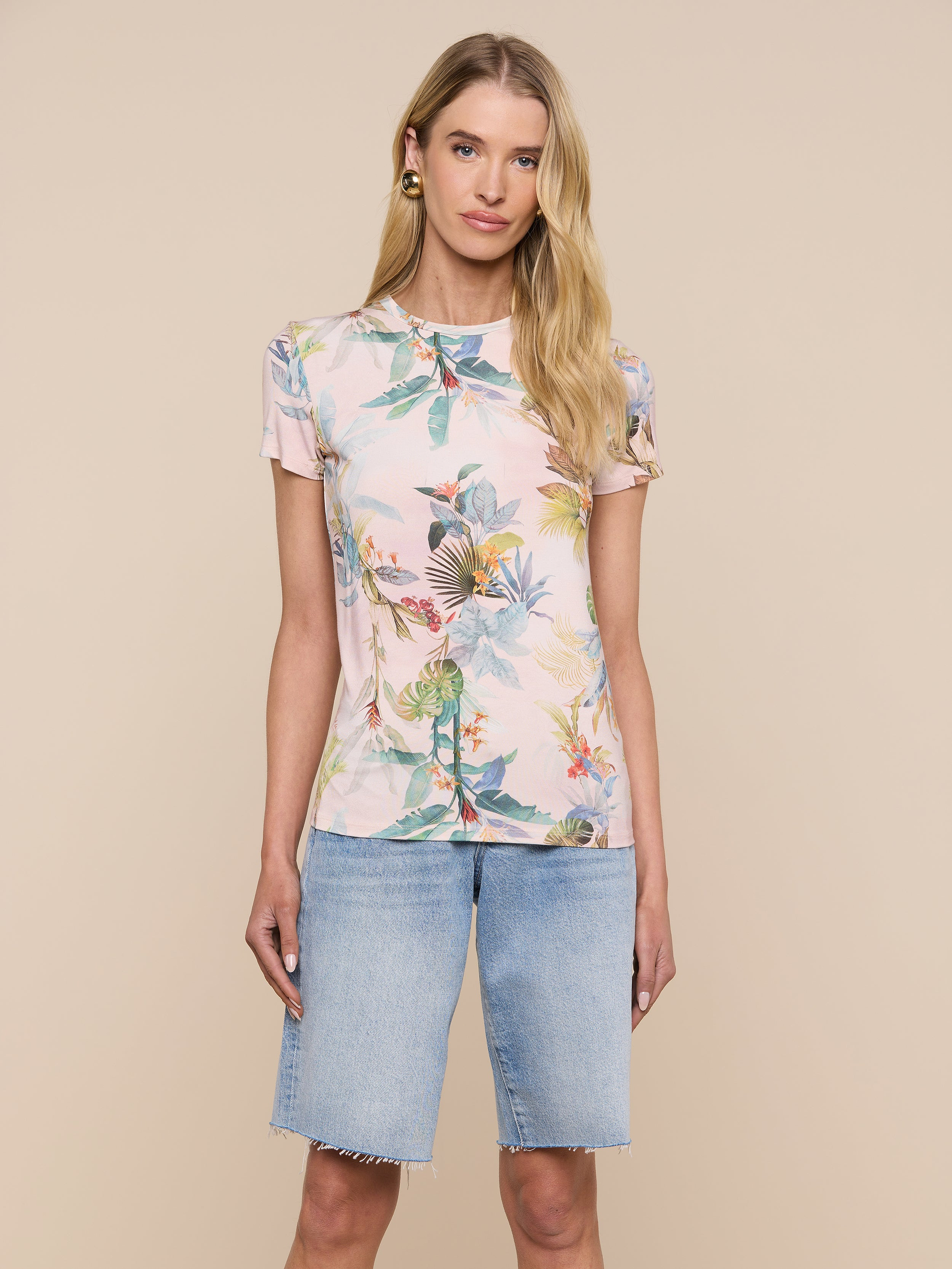 A woman wearing the bestselling Ressi Fitted Tee with a pastel floral print and light blue denim Bermuda shorts stands against a plain white background, looking at the camera with a neutral expression.