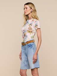 Woman standing in profile against a light background, wearing the Ressi Fitted Tee—a slim-cut pastel floral short-sleeve top—tucked into knee-length denim shorts with a tan belt and gold hoop earrings.