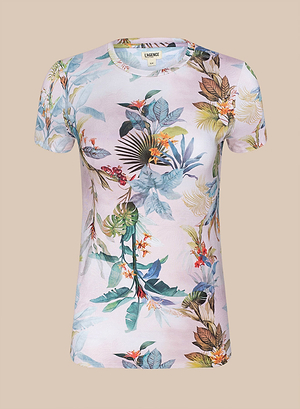 The Ressi Fitted Tee is a bestselling short-sleeved light pink top with a colorful tropical floral pattern of green, blue, and brown palm leaves and orange flowers, shown on a plain beige background.
