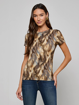 Woman with long dark hair wears the bestselling Ressi Fitted Tee in a feather-patterned stretch jersey with brown and gold tones, paired with blue jeans, standing against a plain light grey background.