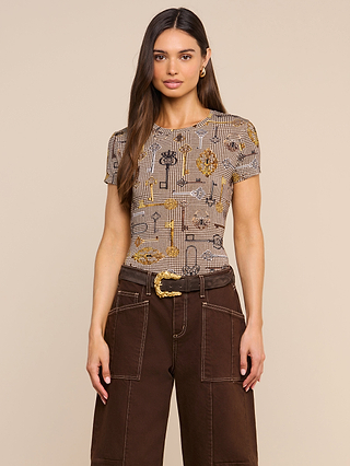 A woman with long brown hair wears the Ressi Fitted Tee in a soft printed jersey and high-waisted brown pants with large pockets, standing against a plain beige background.