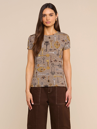 A woman with long brown hair wears the Ressi Fitted Tee, a soft printed jersey slim cut top with a plaid and floral pattern, paired with dark brown pants, standing against a beige background.