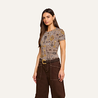 A woman with long brown hair wears the bestselling Ressi Fitted Tee and high-waisted dark brown pants with white stitching, standing against a plain light background.