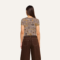 A woman with long brown hair stands facing away, wearing the bestselling Ressi Fitted Tee and high-waisted brown pants with white stitching, against a plain light background.