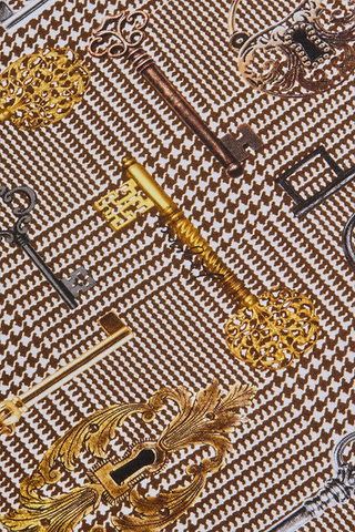 The Ressi Fitted Tee is a slim-cut style made from soft printed jersey, featuring an ornate pattern of vintage keys and keyholes in gold, bronze, and black set against a classic brown houndstooth background.