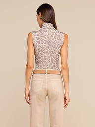 A woman faces away from the camera, wearing the Ceci Sleeveless Turtleneck in a grey leopard print paired with beige pants featuring visible back pockets, set against a plain light background.