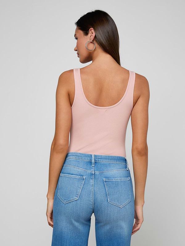 Woman with long brown hair and large hoop earrings, wearing the Nica Scoopneck Bodysuit in light pink high stretch rib and blue high-waisted jeans, shown from the back against an off-white background.