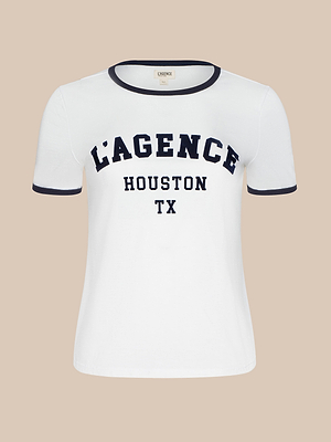 The Tommie Crewneck Tee offers a relaxed fit, made from soft Supima cotton. It features bold navy L’AGENCE HOUSTON TX text on the front, with navy trim on the collar and sleeves against a plain beige background.