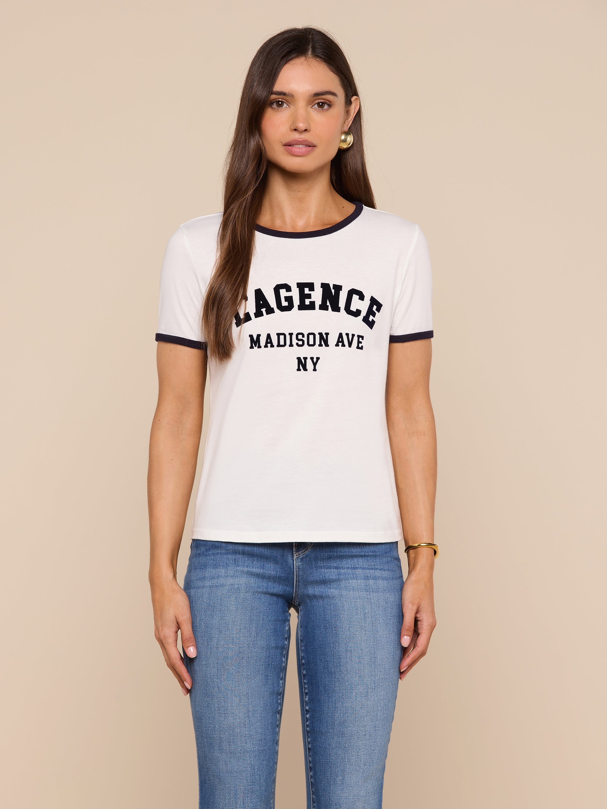 Woman with long brown hair wears a relaxed fit Tommie Crewneck Tee made from Supima cotton and blue jeans, standing against a beige background.