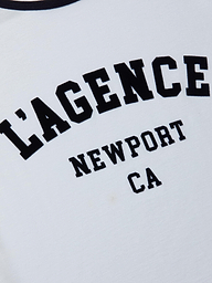 Introducing the Tommie Crewneck Tee: a white ringer tee featuring black text with “LAGENCE” in large letters and “NEWPORT CA” in smaller print underneath. Crafted from soft Supima cotton, it offers a relaxed fit for all-day comfort.