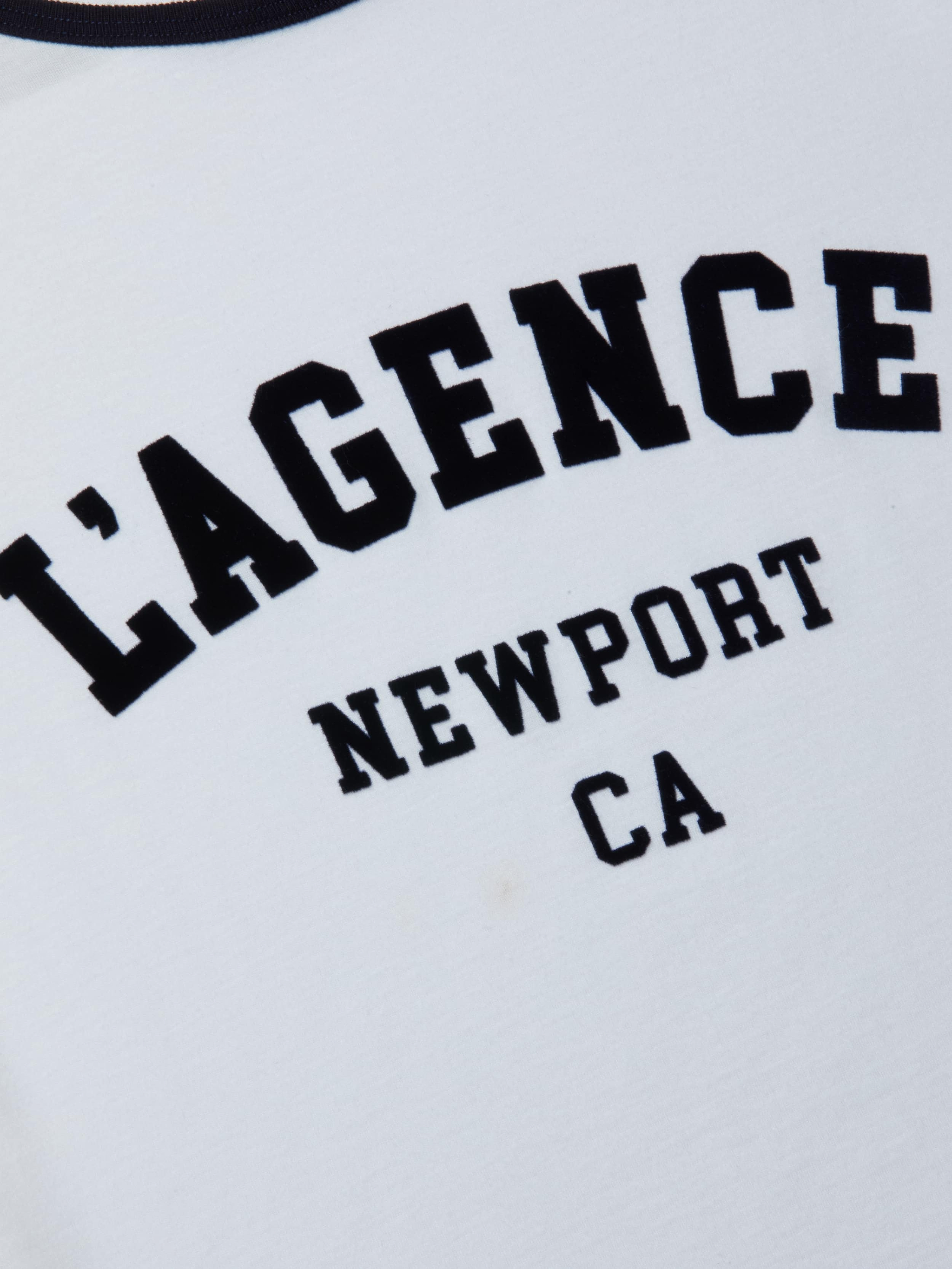 Introducing the Tommie Crewneck Tee: a white ringer tee featuring black text with “LAGENCE” in large letters and “NEWPORT CA” in smaller print underneath. Crafted from soft Supima cotton, it offers a relaxed fit for all-day comfort.