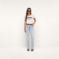 A woman stands against a plain white background wearing sunglasses, light blue jeans with a black belt, black sandals, and the white Tommie Crewneck Tee made from Supima cotton.