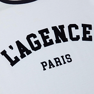 A close-up of the Tommie Crewneck Tee, crafted from white Supima cotton and featuring bold, collegiate-style black text that reads LAGENCE PARIS.