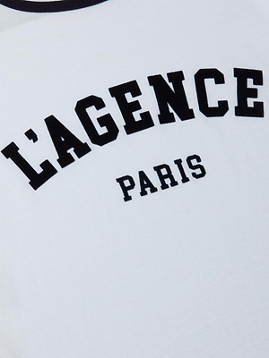 The image shows the Tommie Crewneck Tee in white Supima cotton, featuring bold black LAGENCE text and PARIS in smaller letters below. The tee has a relaxed fit and a minimalist design.