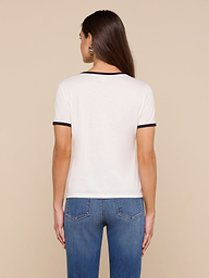 A woman with long brown hair stands facing away, wearing the Tommie Crewneck Tee—crafted from soft Supima cotton in a relaxed fit—paired with blue jeans against a plain light background.