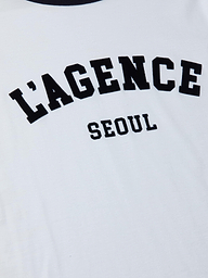 The Tommie Crewneck Tee is a relaxed fit white ringer tee crafted from Supima cotton, featuring bold black “LAGENCE” lettering across the front with “SEOUL” printed in smaller letters underneath.