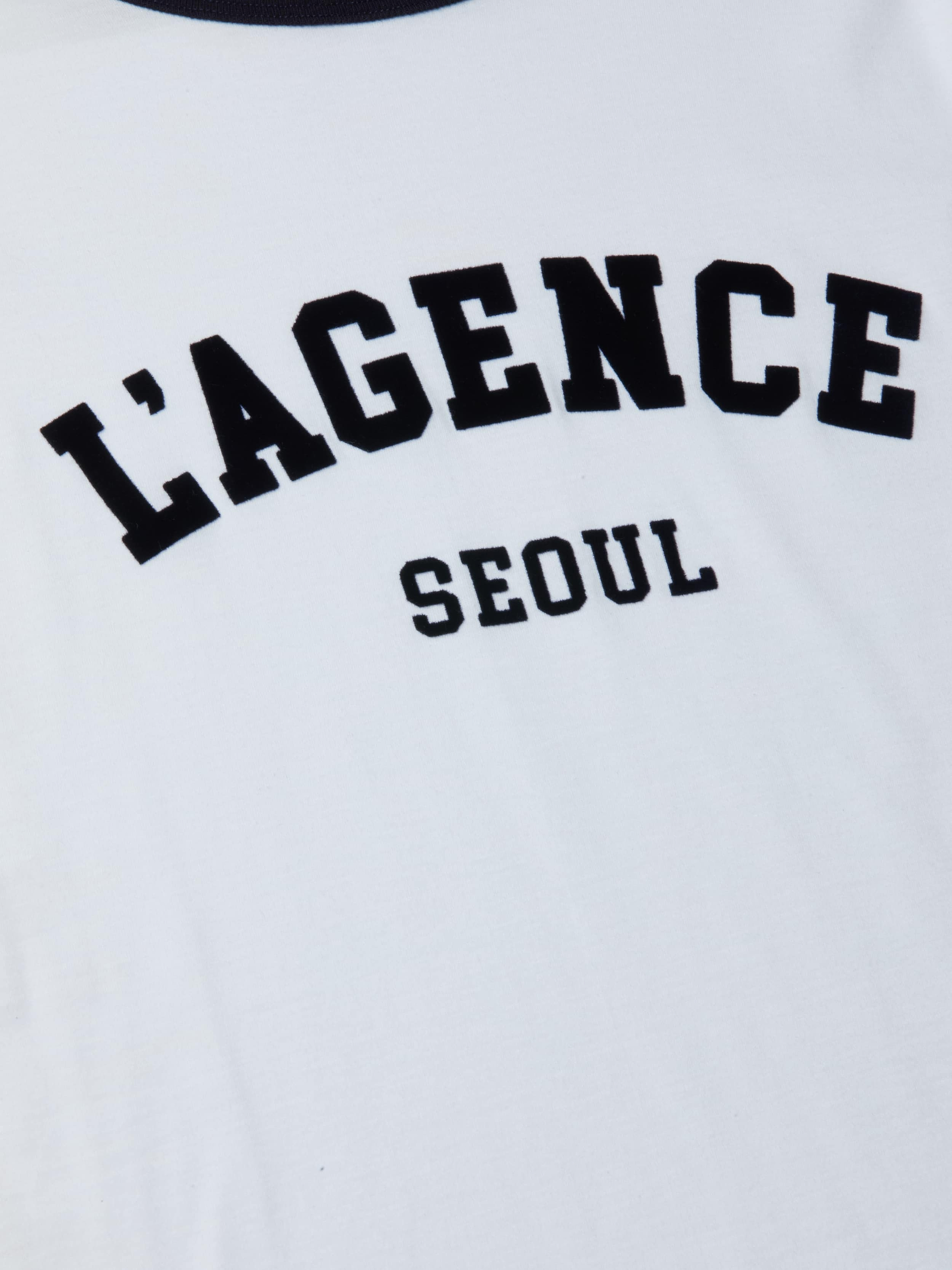 The Tommie Crewneck Tee is a relaxed fit white ringer tee crafted from Supima cotton, featuring bold black “LAGENCE” lettering across the front with “SEOUL” printed in smaller letters underneath.