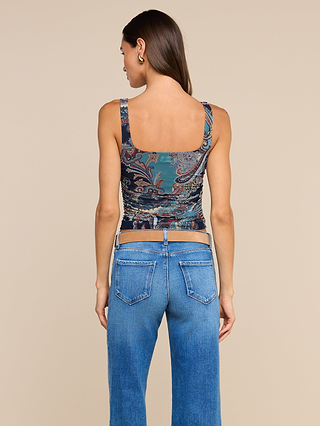 A woman stands facing away, wearing the Rasha Shirred Mesh Tank with a shirred waist and square neckline, paired with blue jeans against a plain beige background.