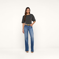 A woman stands against a plain white background wearing the Daria Oversized Cropped Tee in dark gray with blue jeans, a yellow belt, and tan shoes. She has long, straight hair and one hand in her pocket.