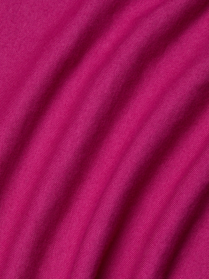 Close-up of magenta organic cotton fabric from the Zeva Tee, showing visible texture and soft diagonal folds that create gentle shadows across the surface.