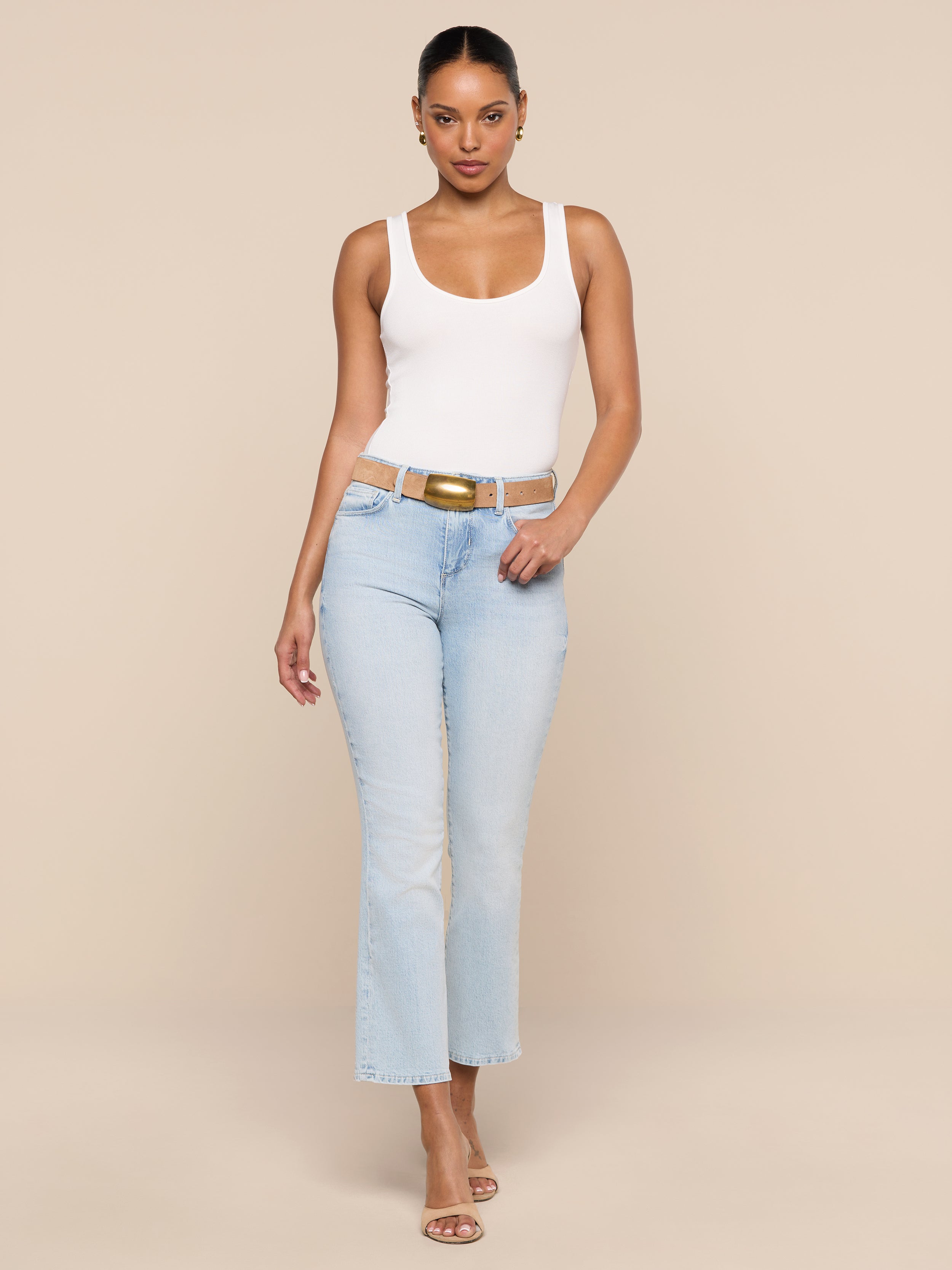 A woman in the Cole Scoopneck Tank and light blue jeans with heeled sandals stands against a plain white background, walking confidently toward the camera.