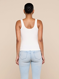 A person with dark hair in a bun wears the Cole Scoopneck Tank in white and light blue jeans, standing with their back to the camera against a plain light background.