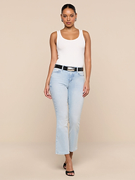 A person wearing the Nyra Bodysuit in white as a base layer, paired with light blue jeans, a black belt, and black heels, stands against a plain white background facing forward with a neutral expression.