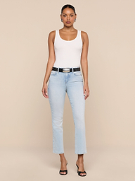A woman stands facing forward wearing the Nyra Bodysuit as a soft stretch rib base layer, paired with light blue jeans, a black belt, and black open-toe heels against a plain white background.