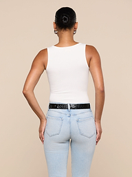 A person with their hair in a bun is seen from the back, wearing the Nyra Bodysuit—a white sleeveless soft stretch rib top—paired with light blue jeans and a black belt, standing against a plain light background.