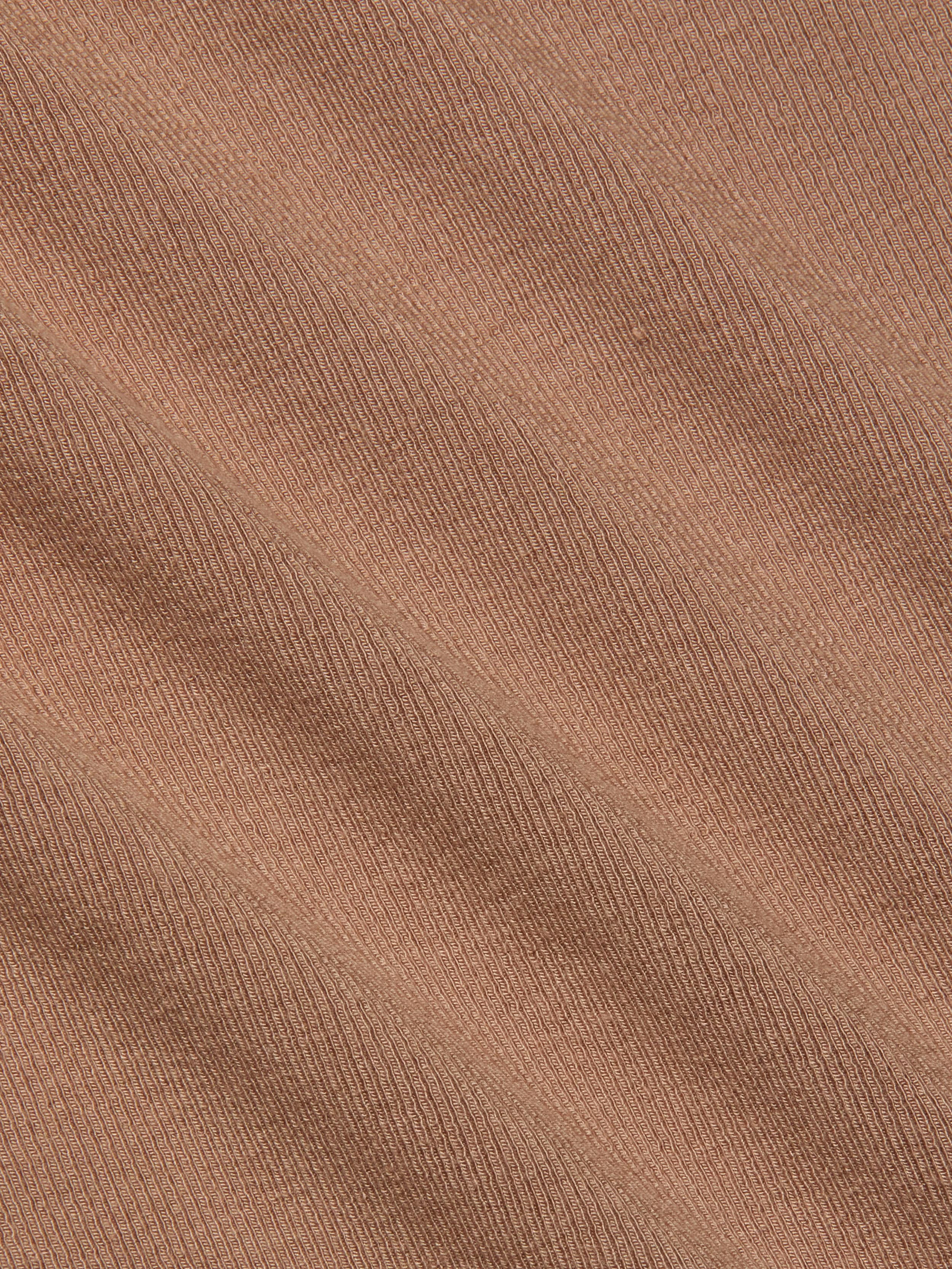 Close-up of the Wrenna Racerback Bodysuit’s light brown rib fabric, featuring fine, evenly spaced diagonal ridges and visible texture. The material showcases a subtle pattern with soft shadow effects across its surface.