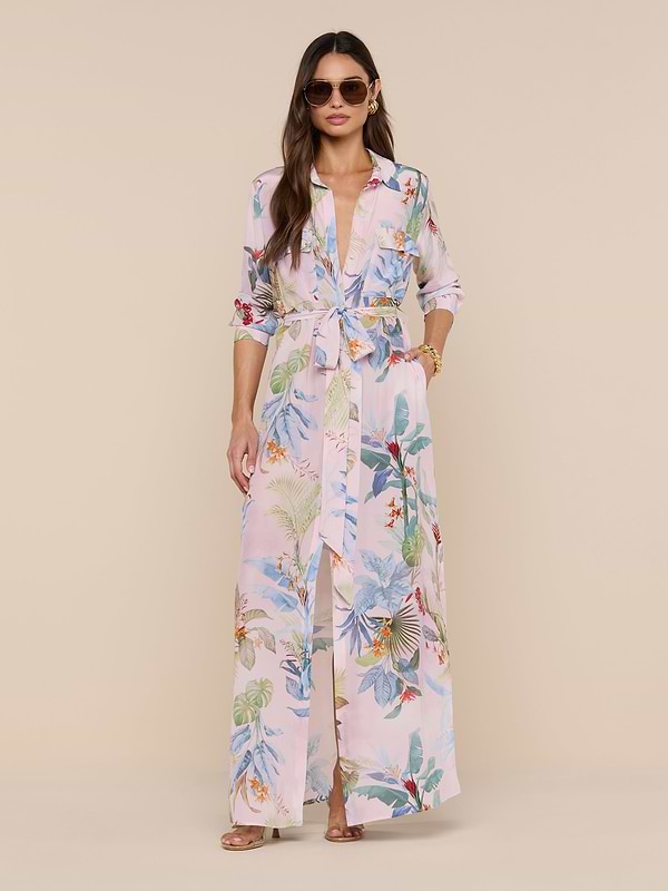Woman in sunglasses and the Cameron Silk Shirt Dress—featuring a belted waist and rolled-up sleeves—stands against a beige background with loose hair, bracelets, and rings.