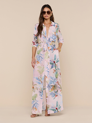 Woman in sunglasses and the Cameron Silk Shirt Dress—featuring a belted waist and rolled-up sleeves—stands against a beige background with loose hair, bracelets, and rings.