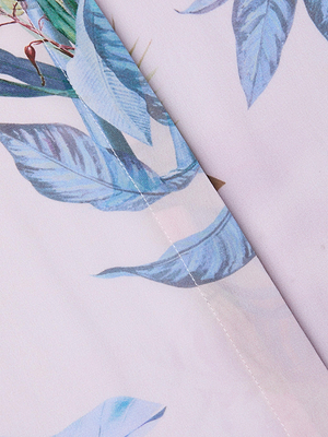 Close-up of the Cameron Silk Shirt Dress shows light pink crepe de chine silk with blue and green palm leaf print and a diagonal seam detail.