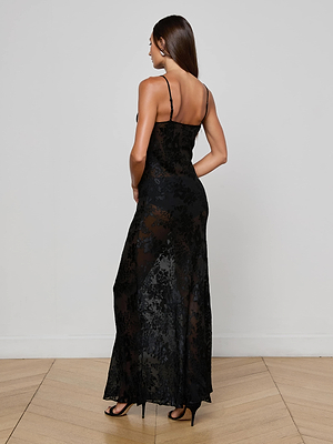 A woman with long brown hair wears the L'AGENCE Christine Burnout Satin Dress and black heels, standing on light wood flooring and facing away from the camera against a plain white wall.