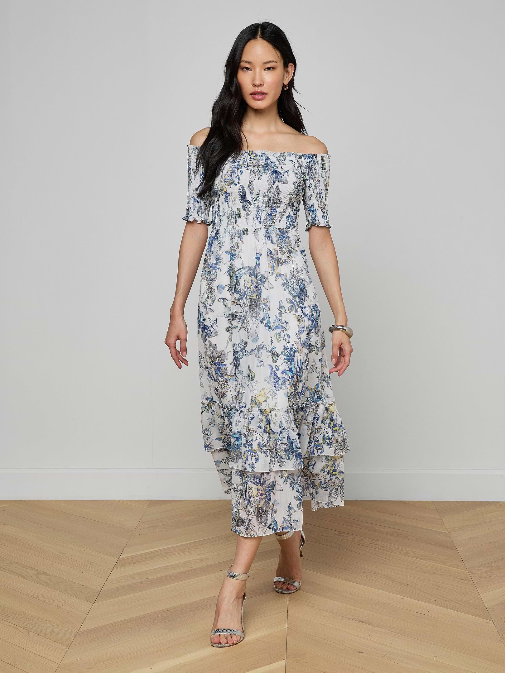 A woman wearing the Oriel Off-Shoulder Dress and sandals stands against a plain light background.
