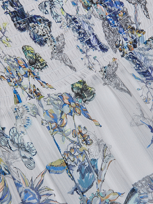 Close-up of the Oriel Off-Shoulder Dress in white, showcasing delicate blue, green, and yellow floral and butterfly print, with smocked stitching near the top and fine detailing on various flowers and branches.