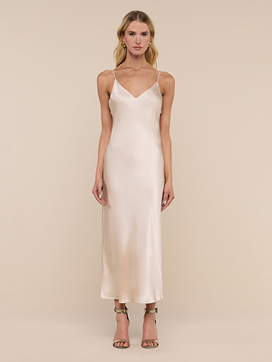 A woman stands facing forward, wearing the Seridie Silk Slip Dress in champagne with thin straps and open-toe heels against a plain beige background.
