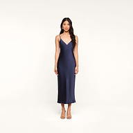 A woman wearing the Seridie Silk Slip Dress—a navy blue, sleeveless, V-neck midi dress with thin straps—stands against a plain white background, facing forward with a neutral expression, making it an elegant choice for a wedding guest.
