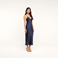 A woman wearing the Seridie Silk Slip Dress in navy blue and heels stands against a plain white background, gazing at the camera with a relaxed expression.