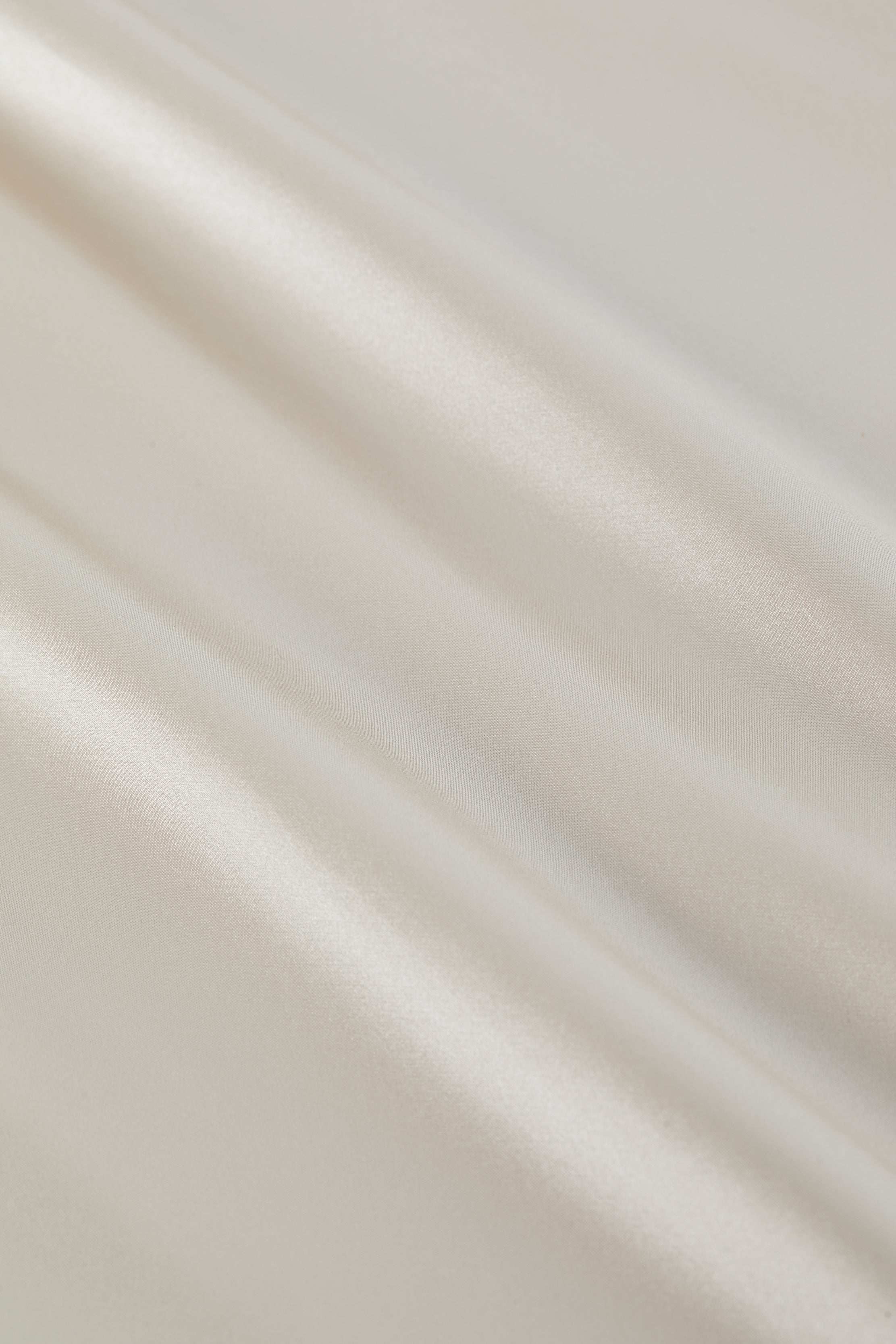 Smooth, shiny ivory fabric with gentle, flowing folds and a soft, satin-like texture reflecting light—ideal for the Seridie Silk Slip Dress or any bias-cut champagne silk dress.