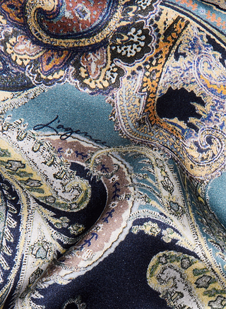 Eine Nahaufnahme des lebhaften, aufwendig gearbeiteten Stoffes mit Mitternachtsblau-Paisley-Muster des Seridie-Seiden-Slip-Kleids, der sich durch wirbelnde Muster in Blau, Gold, Creme und Braun auszeichnet, in die das Markenzeichen dezent eingewebt ist.