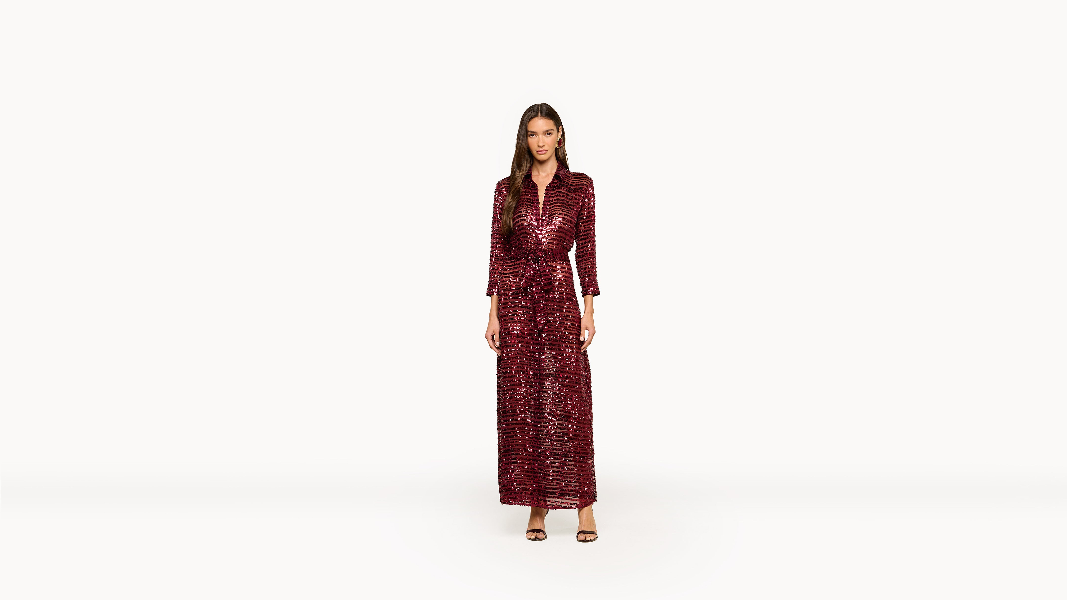 Woman wearing a stunning long red sequin dress with three-quarter sleeves and black high-heeled sandals, standing against a plain white background.